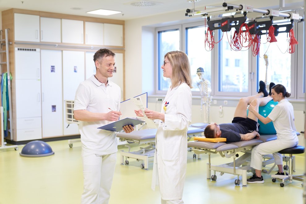 Physiotherapeut spricht mit einer Ärztin über therapeutische Maßnahmen